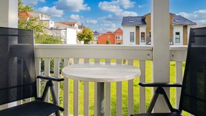 Un balcon avec une table et des chaises, donnant sur une rangée de maisons, avec un ciel bleu dégagé.