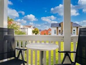 Un balcon avec une table et des chaises, donnant sur une rangée de maisons, avec un ciel bleu dégagé.