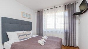Una cama bien hecha con cabecera gris, manta marrón y toallas enrolladas.