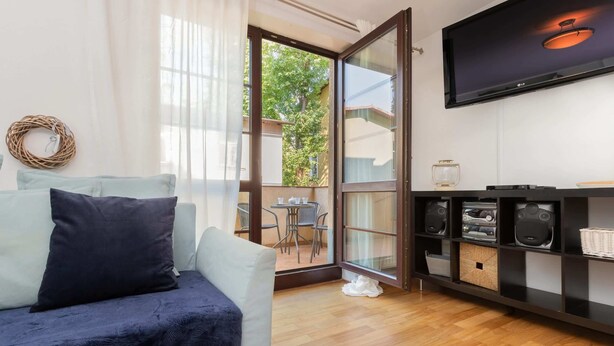 Un salón moderno con un sofá, un televisor instalado en la pared y un ventanal corredero que da a un espacio exterior.