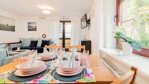 Un comedor con una mesa dispuesta para cuatro, un sofá al fondo y una ventana con vista a zonas verdes.