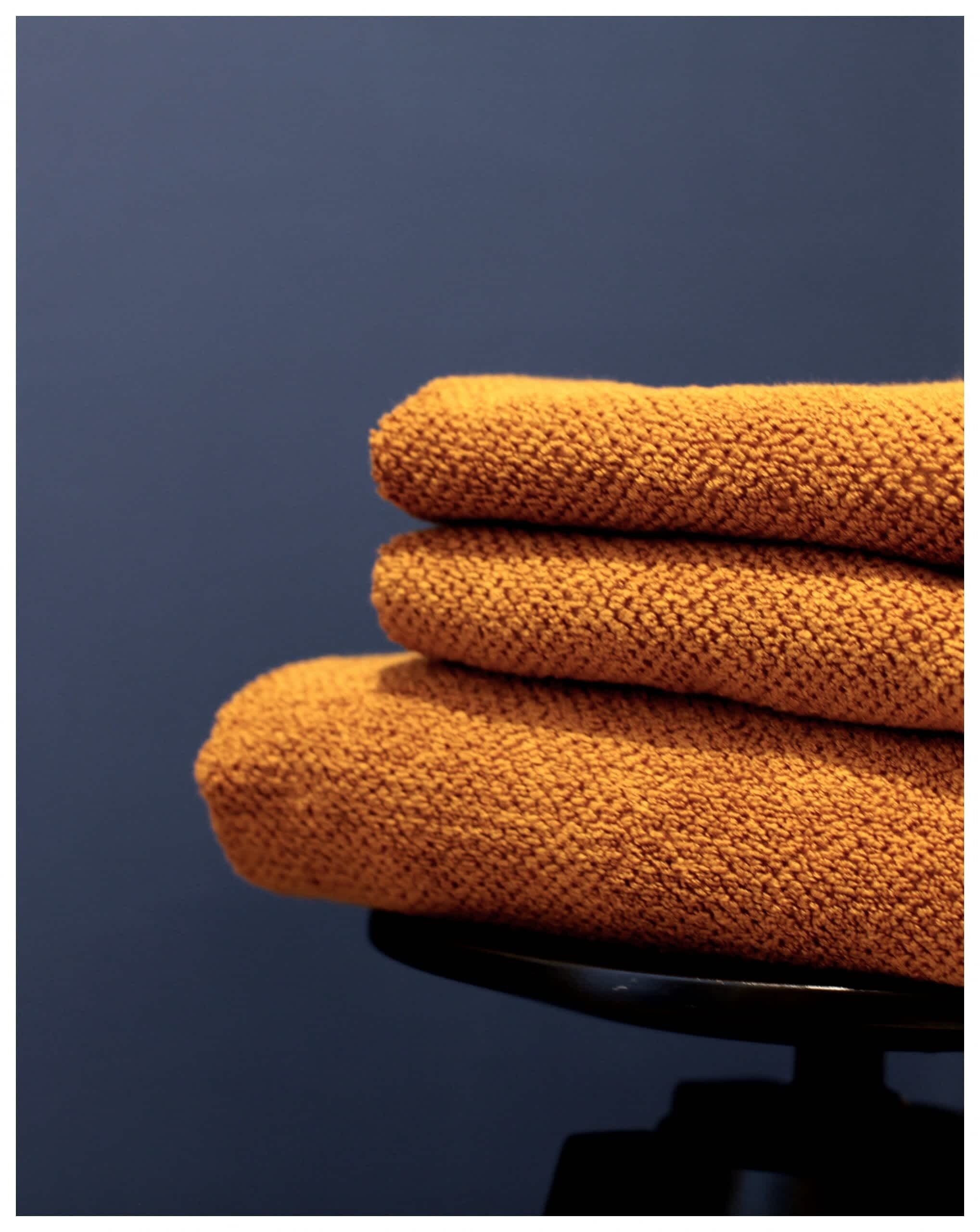 Une pile de serviettes orange est posée sur une chaise noire, le tout se détachant sur un fond bleu foncé.
