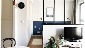 Une pièce avec une télévision, une horloge, une plante et une fenêtre donnant sur la mer.