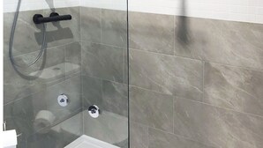 Une douche fermée par des parois en verre, dotée d’un pommeau de douche à main et d’un robinet mural.