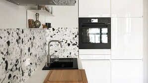 Une cuisine moderne avec un four noir, des meubles blancs et un pare-feu en marbre.