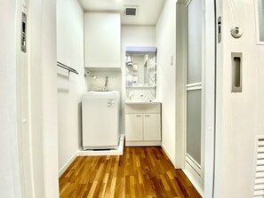 A narrow hallway with a wooden floor, a white refrigerator, a sink, and cabinets.