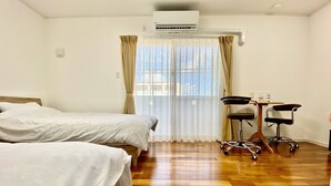 Une chambre d’hôtel avec deux lits, un bureau avec une chaise, un climatiseur et une fenêtre avec des rideaux.