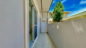 Un couloir étroit avec une porte en verre, une rambarde en métal et un arbre visible à travers la fenêtre.