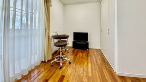 Une pièce avec un plancher en bois, un bureau avec une chaise, une télévision et une armoire.