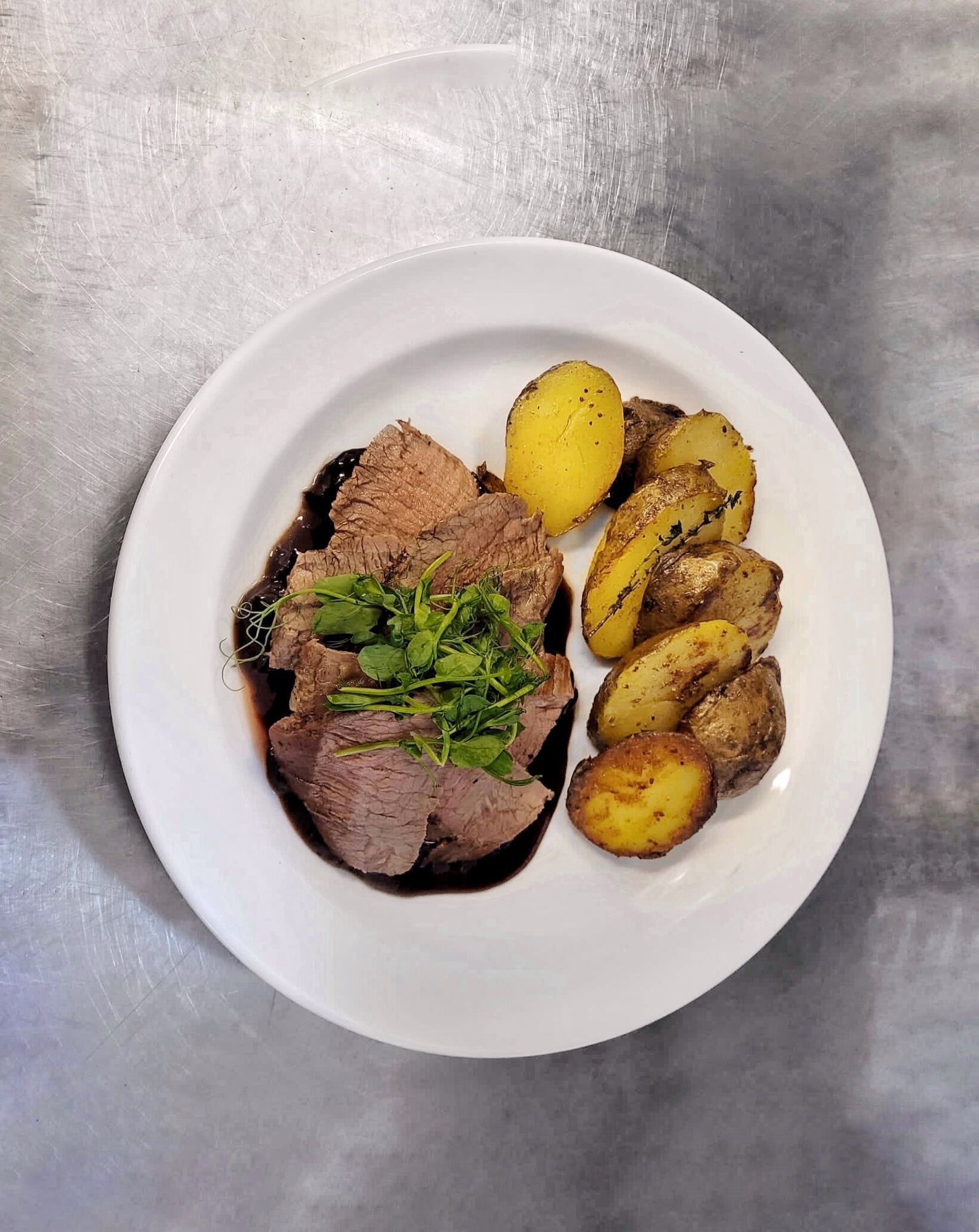 Un plato con carne de res en rodajas y patatas asadas sobre un plato blanco.