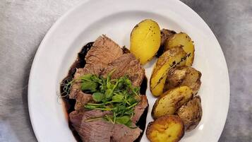 Un plato con carne de res en rodajas y patatas asadas sobre un plato blanco.