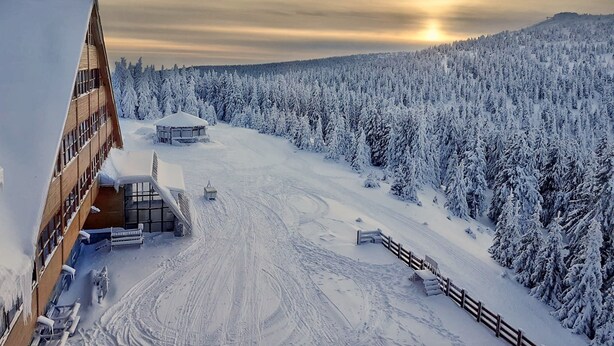 Lumipeitteinen hiihtokeskus, jossa on puinen rakennus, hiihtohissi ja metsäinen vuoristo taustalla.
