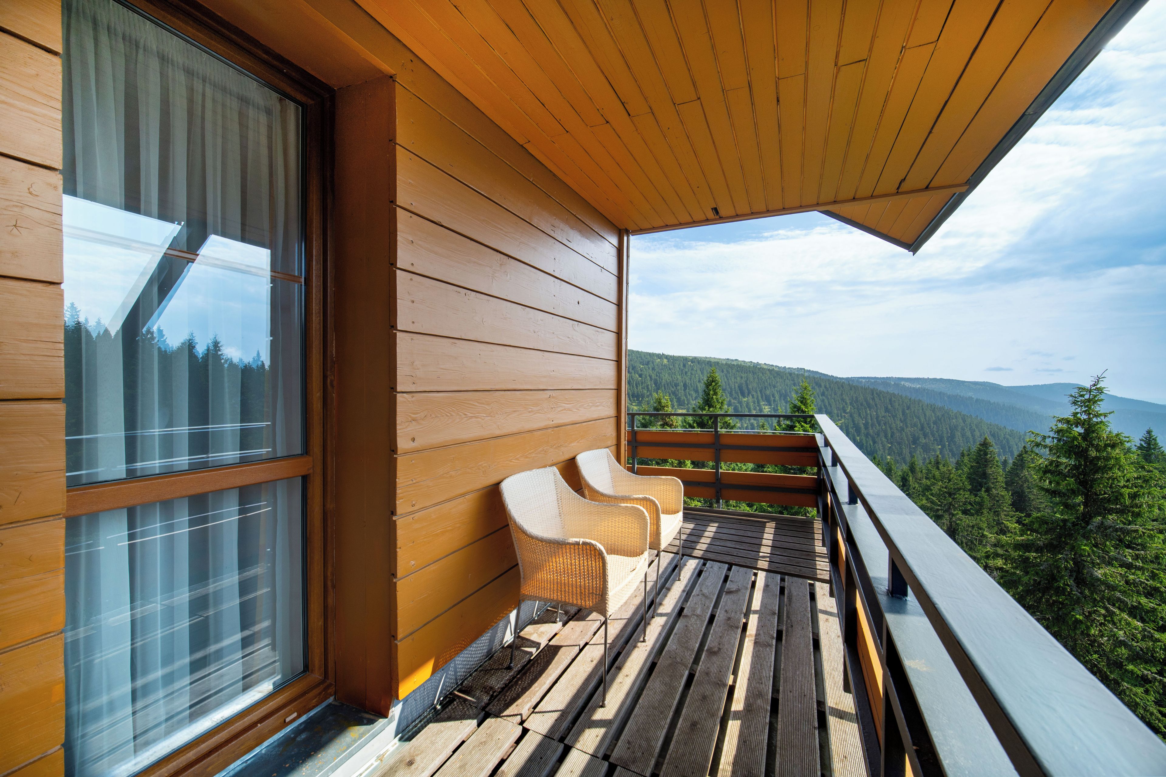 A wooden balcony with a view of a forested mountain range.