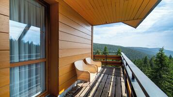 A wooden balcony with a view of a forested mountain range.