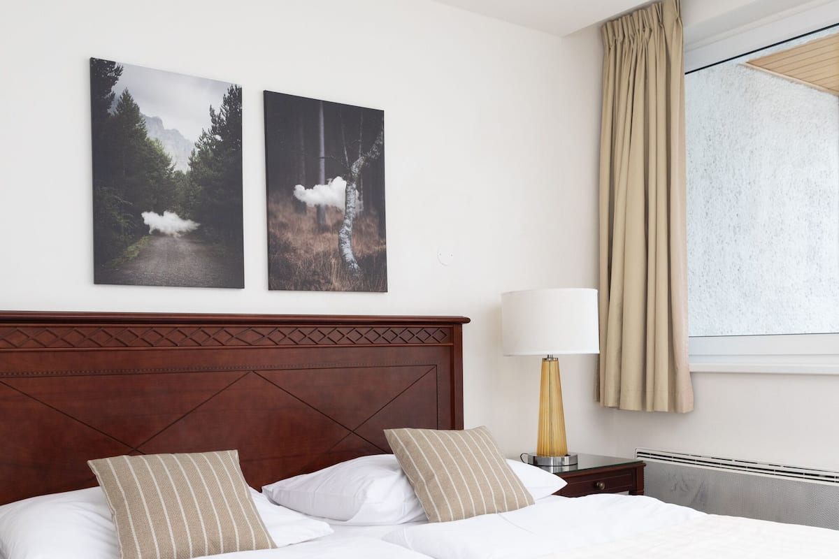 A neatly made bed with white and striped pillows, a wooden headboard, and two framed pictures on the wall.