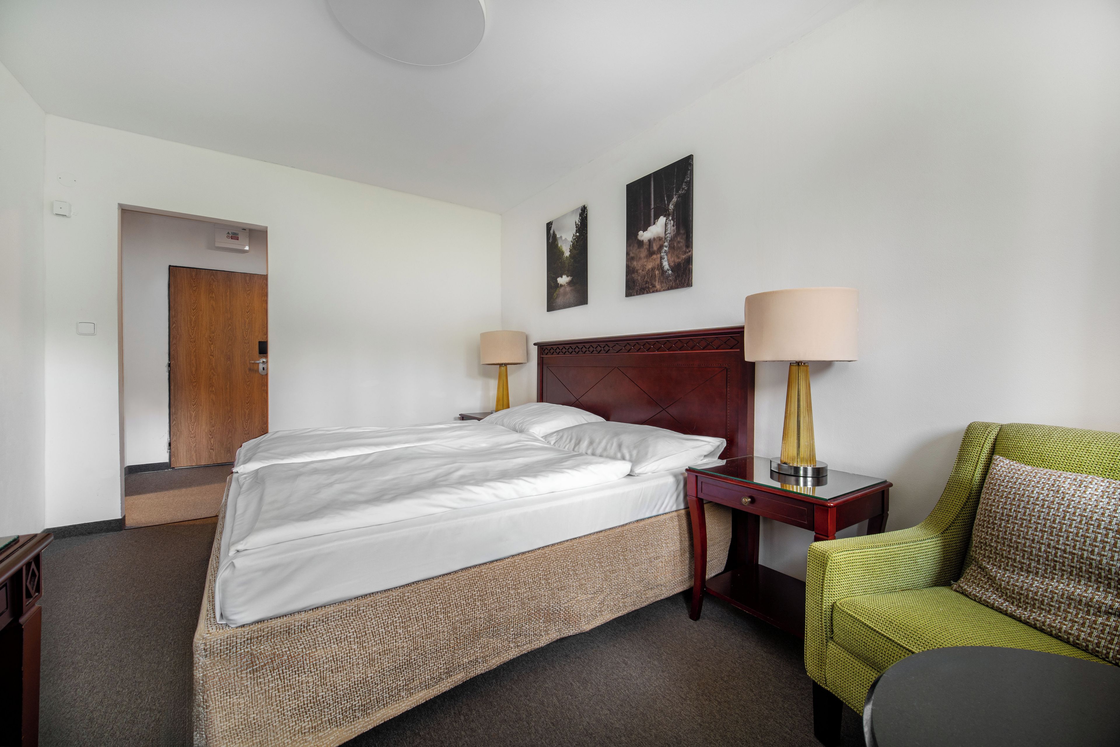 Ein Hotelzimmer mit einem Bett, zwei Nachttischlampen, einem Sessel und zwei gerahmten Bildern an der Wand.