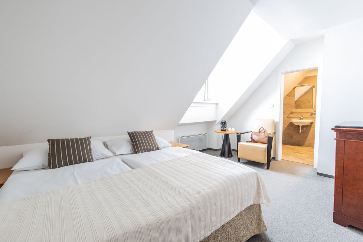 A bedroom with a large bed, a small table with a lamp, a chair, and a wooden cabinet.