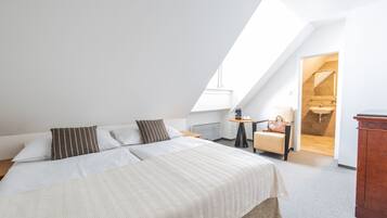 A bedroom with a large bed, a small table with a lamp, a chair, and a wooden cabinet.