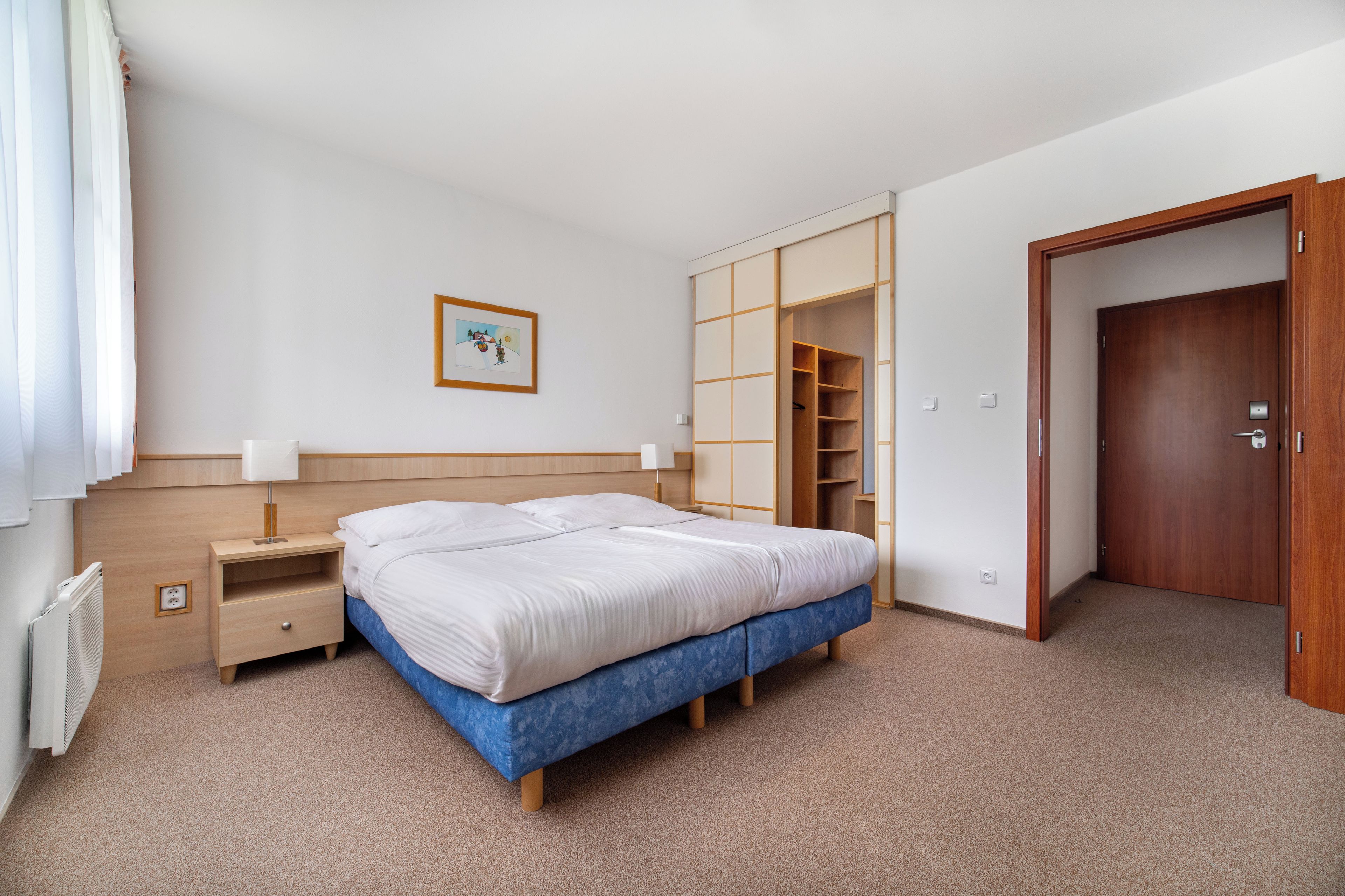 Un dormitorio con cama, mesitas de noche, un armario y una puerta.