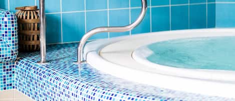 A hot tub with a metal ladder, surrounded by blue-tiled walls and floor.