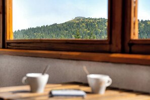 A table with two cups and a smartphone, viewed through a window overlooking a forested hill.