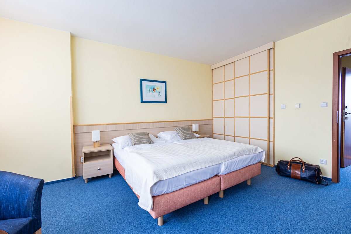 A hotel room with a bed, bedside table, lamp, and a blue carpet.
