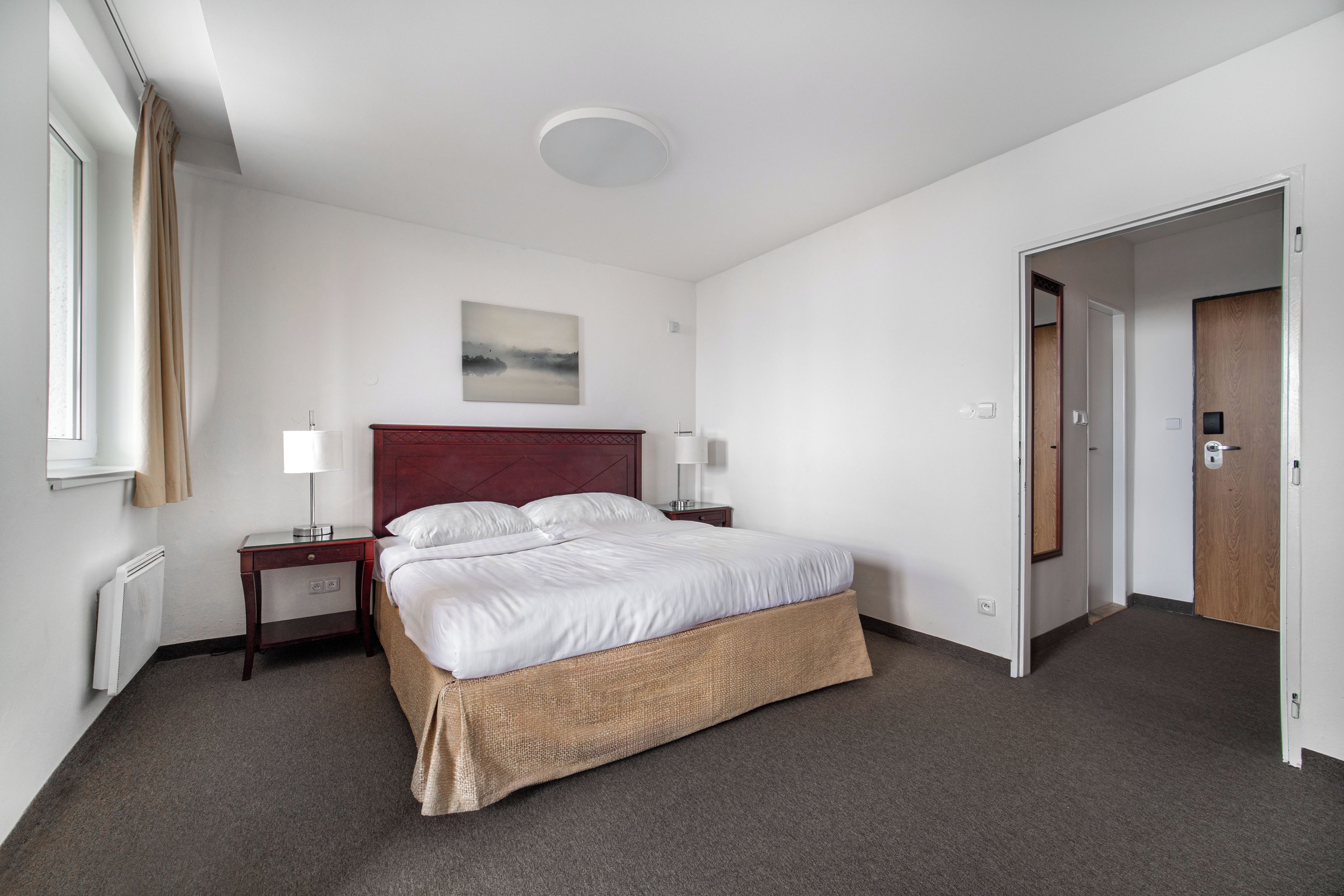Une chambre d’h ôtel avec un lit simple, une table de chevet, une lampe, un tableau au mur et une porte donnant sur une autre pièce.
