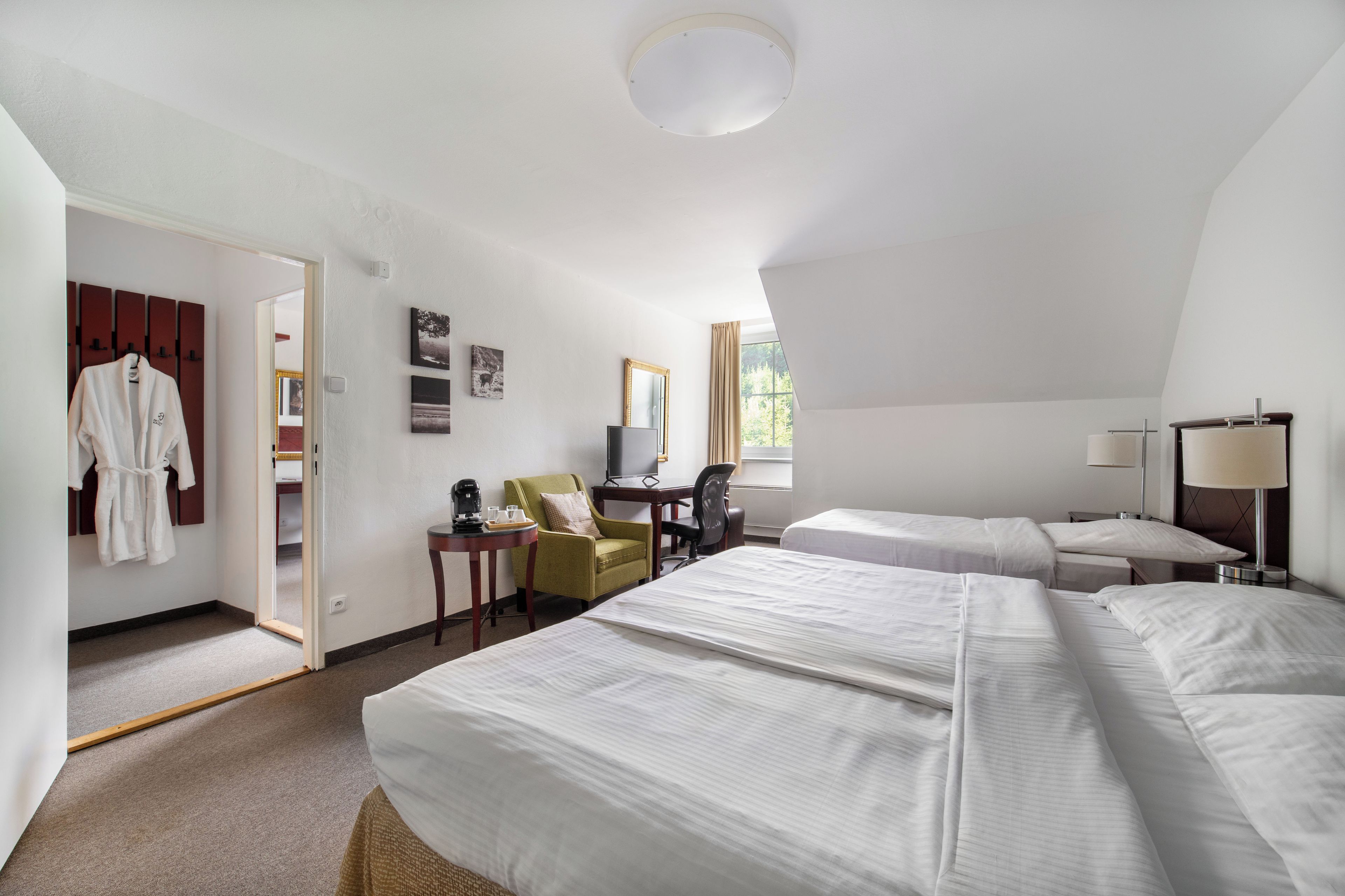 Habitación de hotel con dos camas, un escritorio, una silla, un armario y una ventana con cortinas.