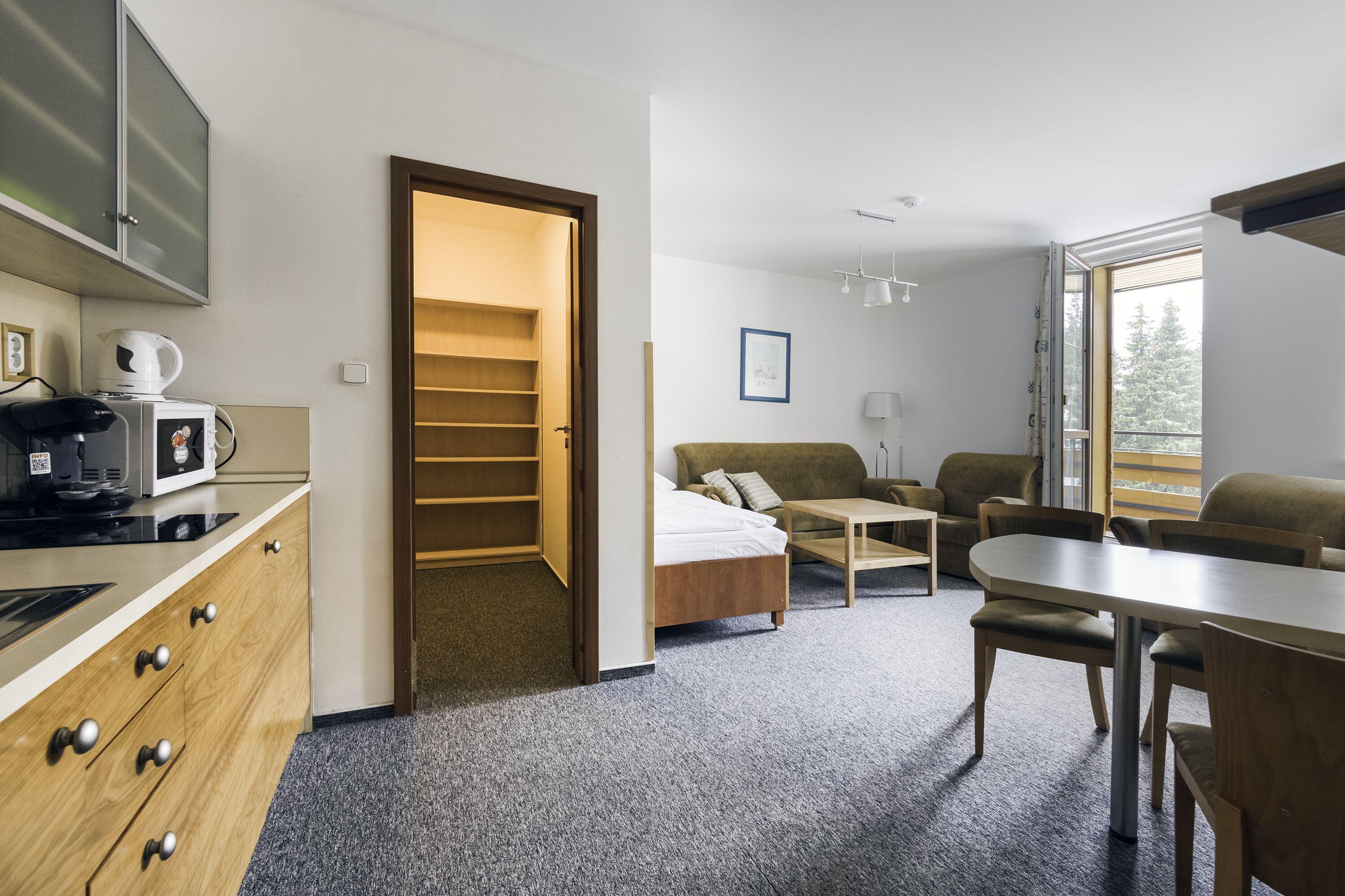 Una habitación de hotel moderna con kitchenette, cama, sofá, mesa de comedor y un amplio ventanal.