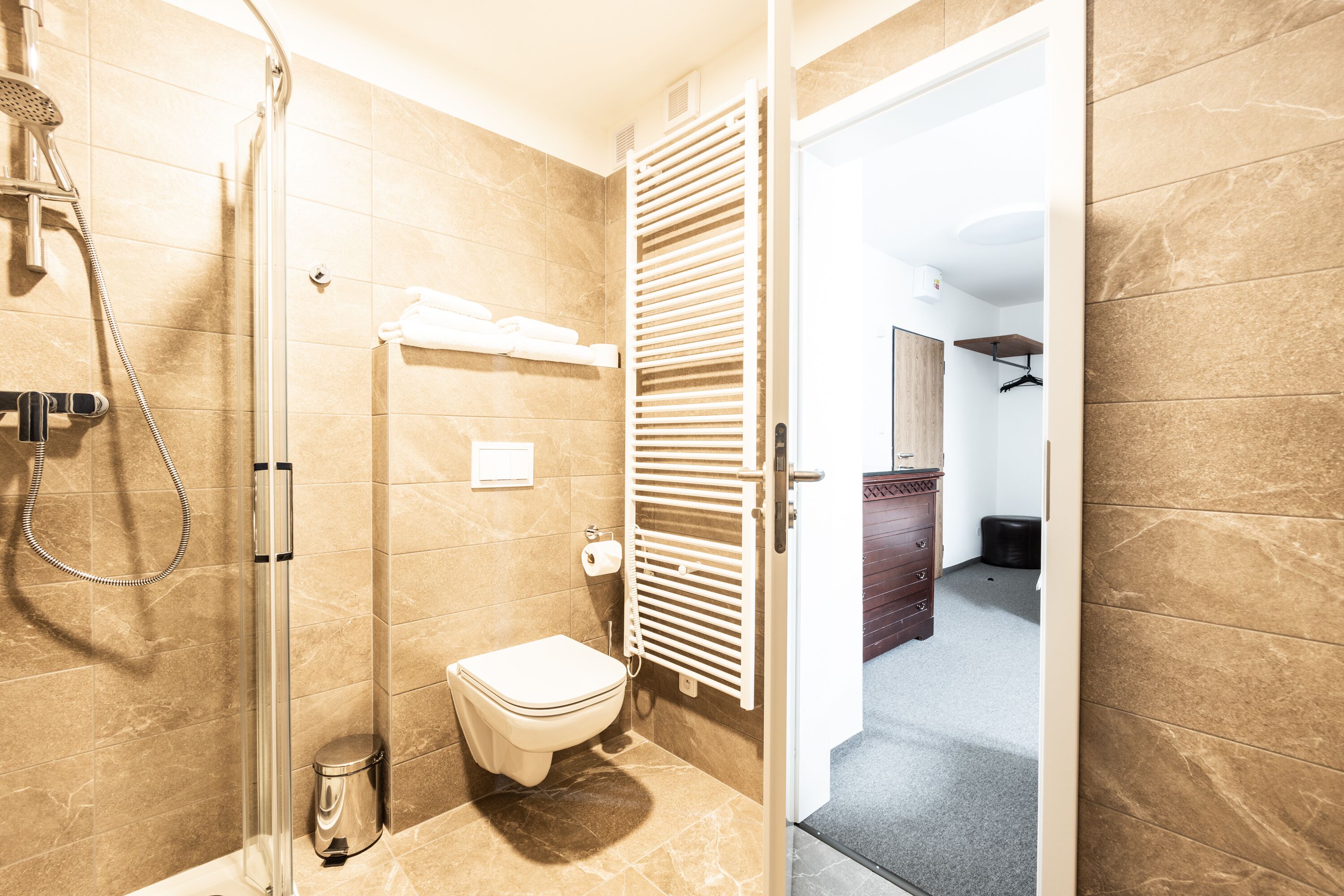 A modern bathroom with a shower, toilet, and towel rack.