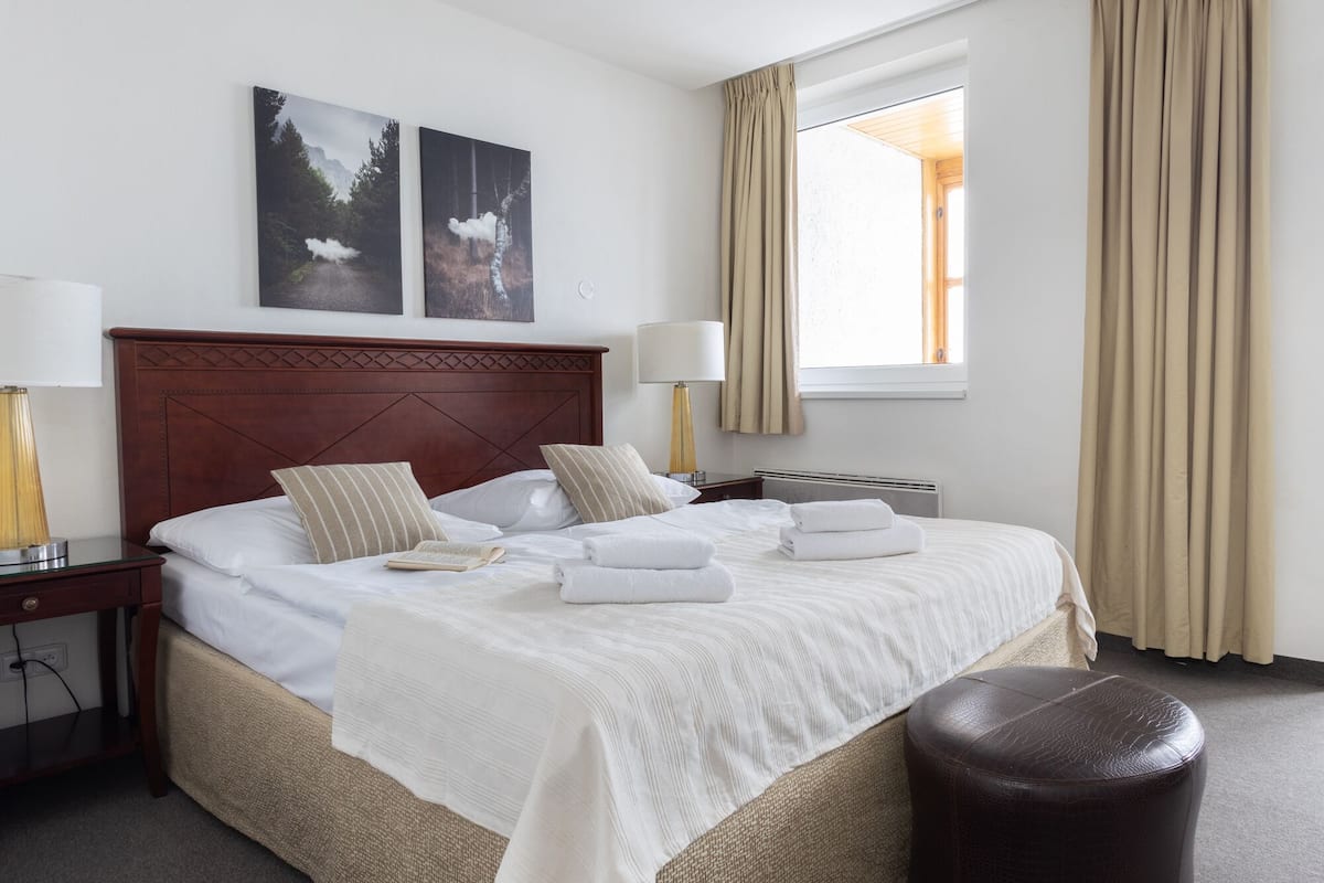 A hotel room with a large bed, two bedside tables, a round ceiling light, and a window with curtains.