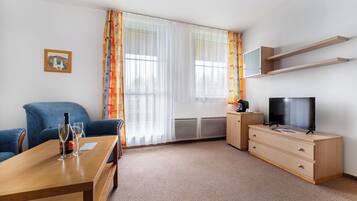 Habitación de hotel con escritorio de madera, televisión, sofá y ventana con cortinas.
