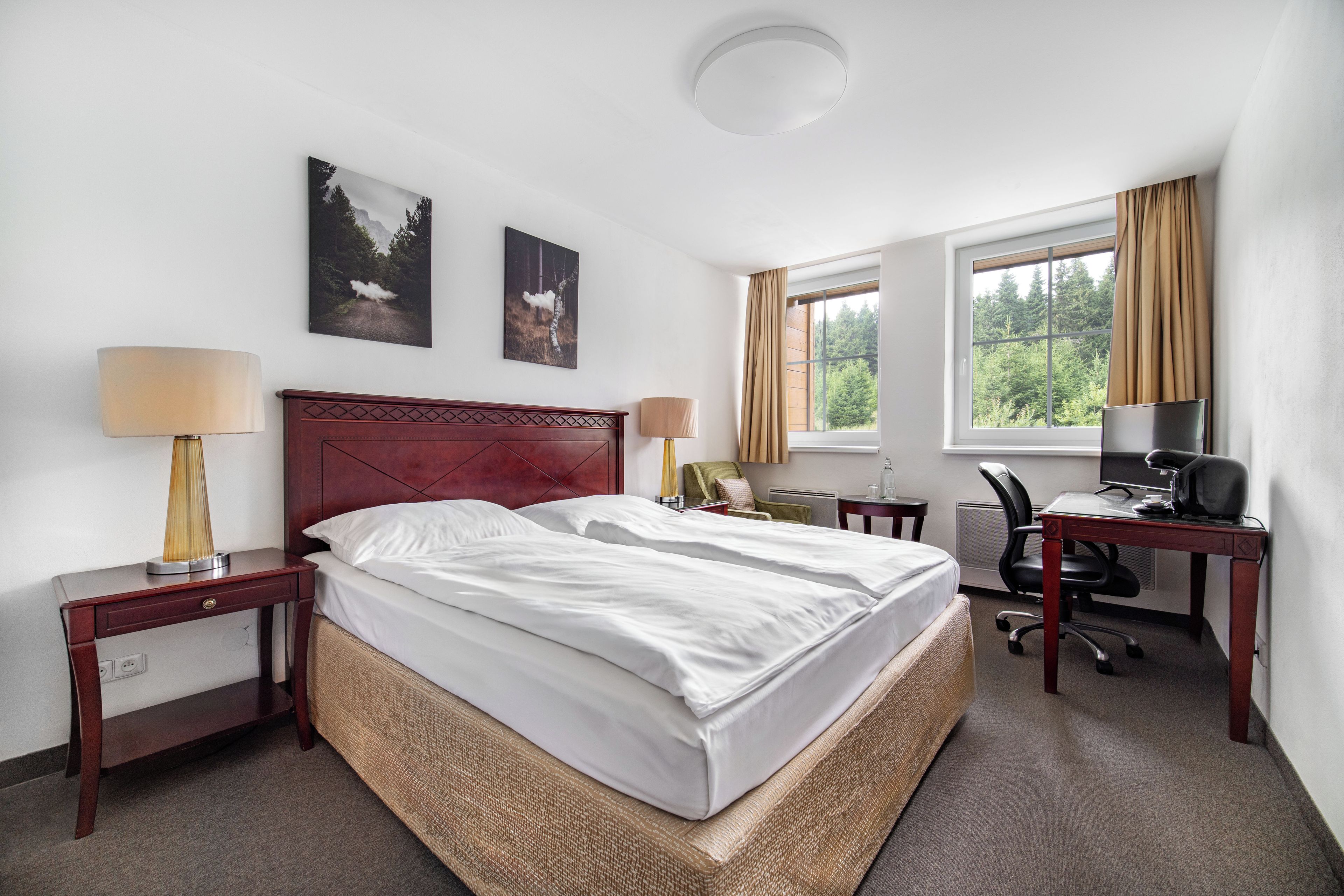 Habitación de hotel con cama doble, escritorio con silla, lámpara y ventana con cortinas.