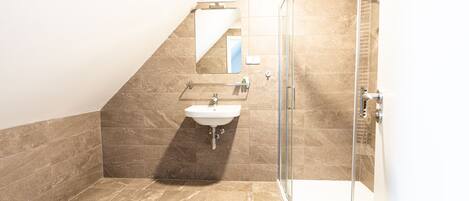 A bathroom with a glass shower enclosure, a sink, and a mirror.