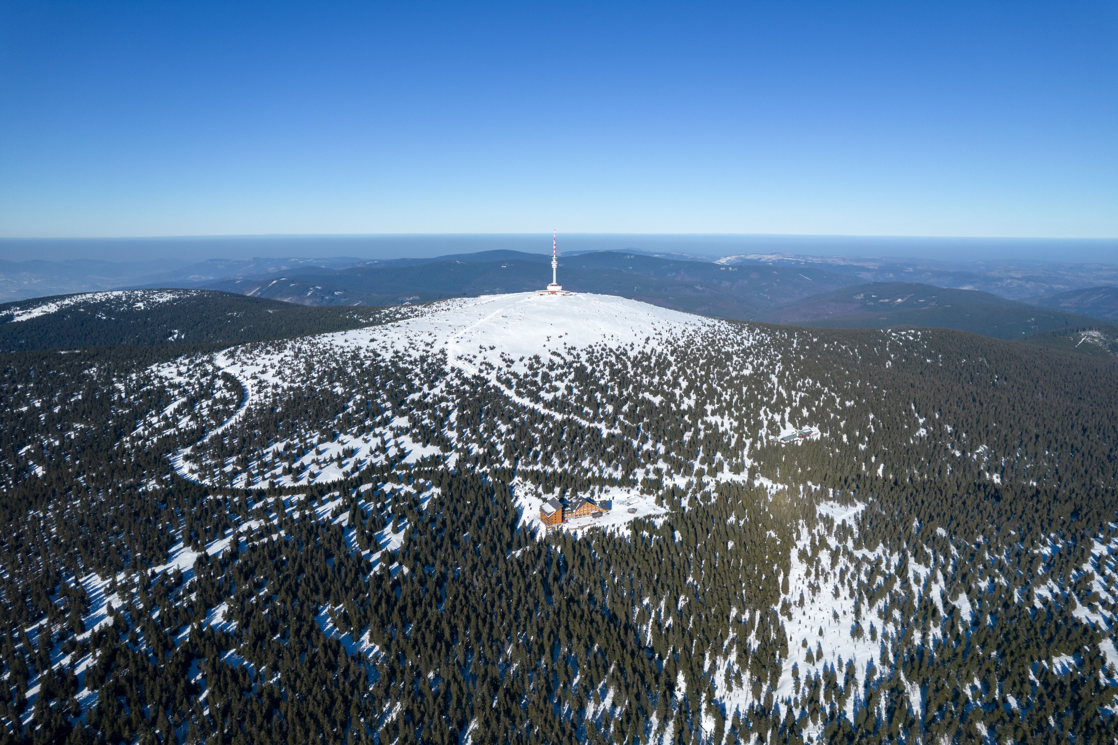 Una montaña nevada con una cabaña y una alta torre blanca en el centro.