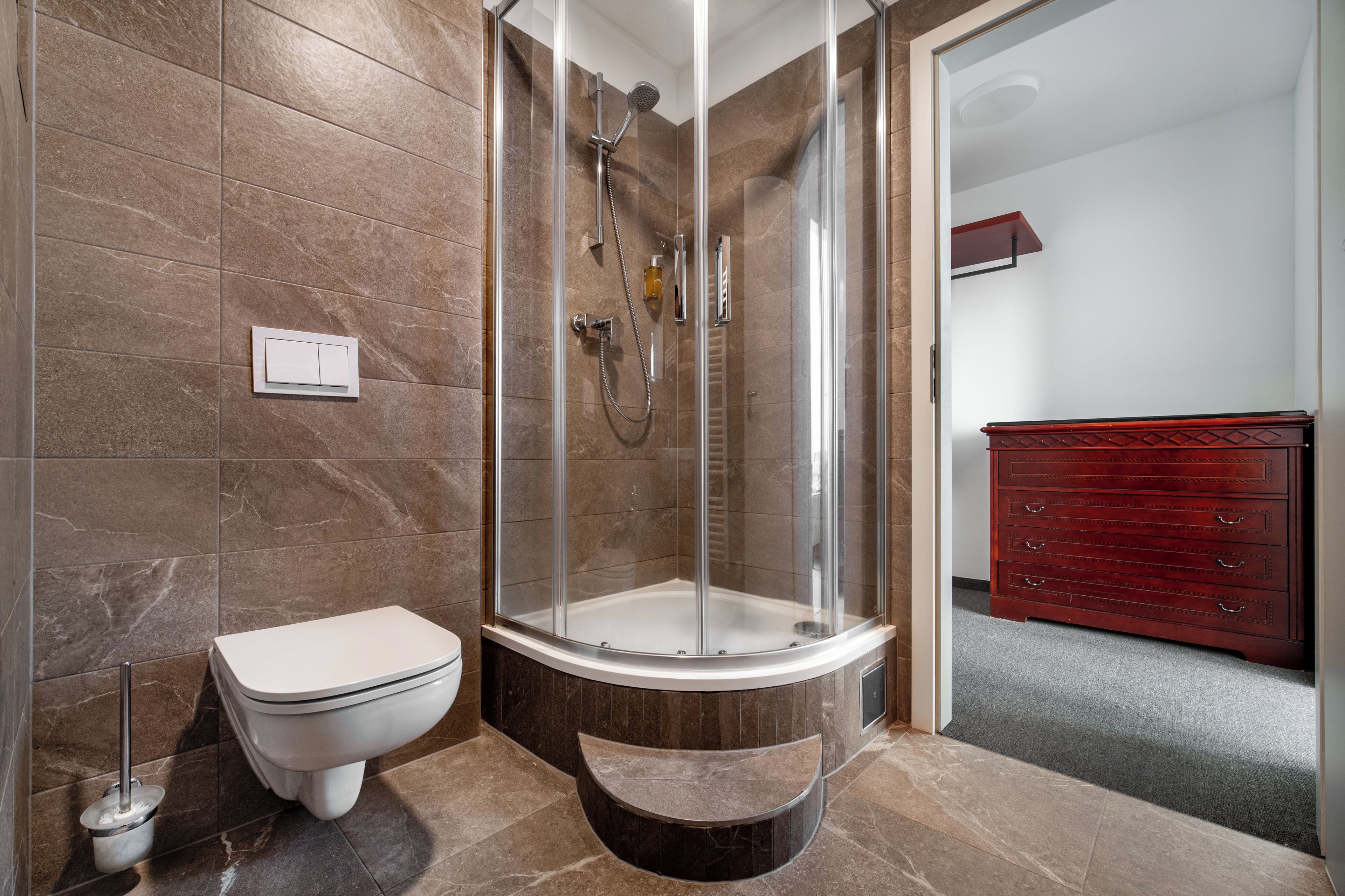 Een badkamer met een douche met glazen wand, een toilet en een wastafel met lades.