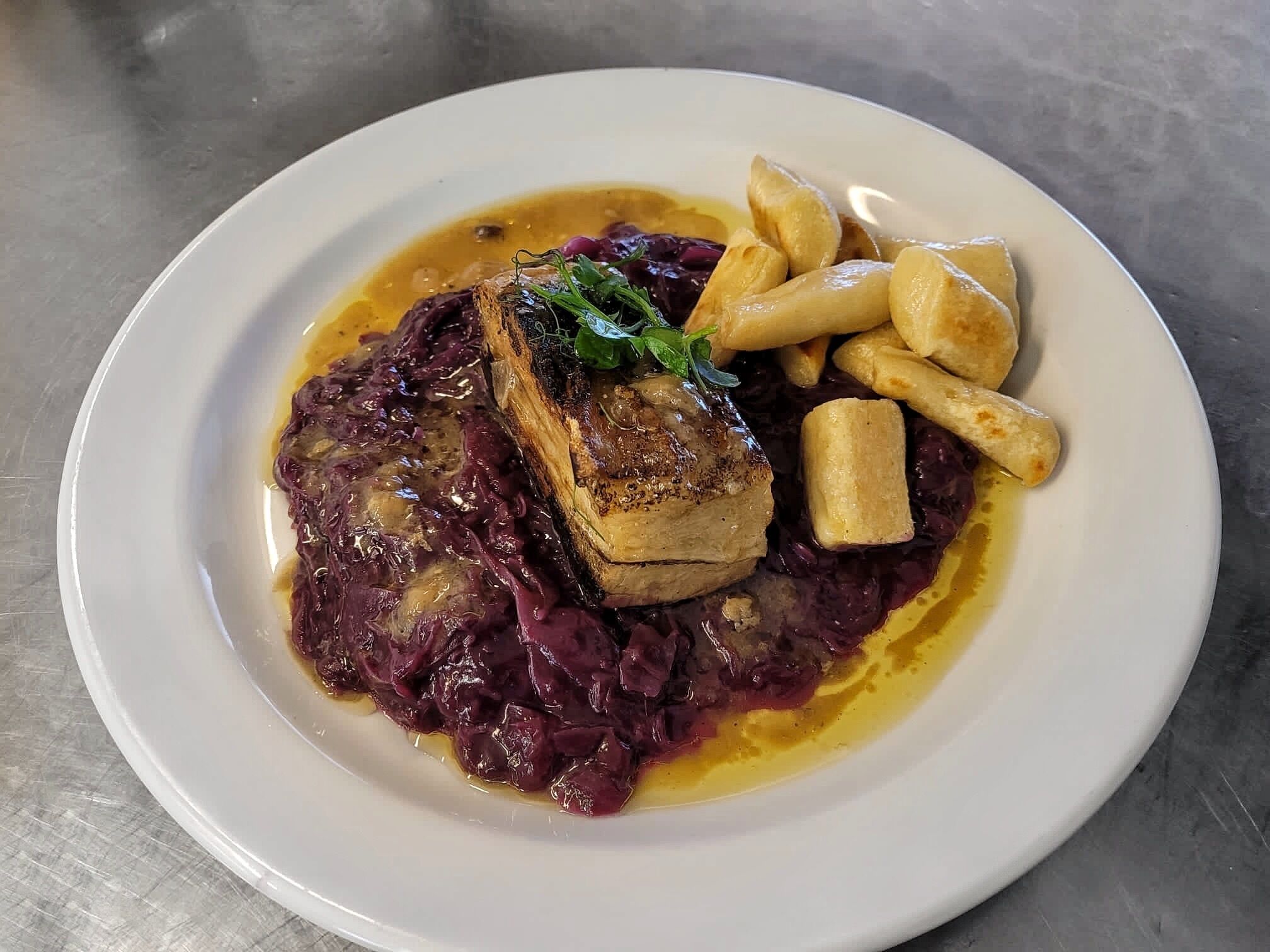 A plate of food with a piece of meat, red cabbage, and fries.