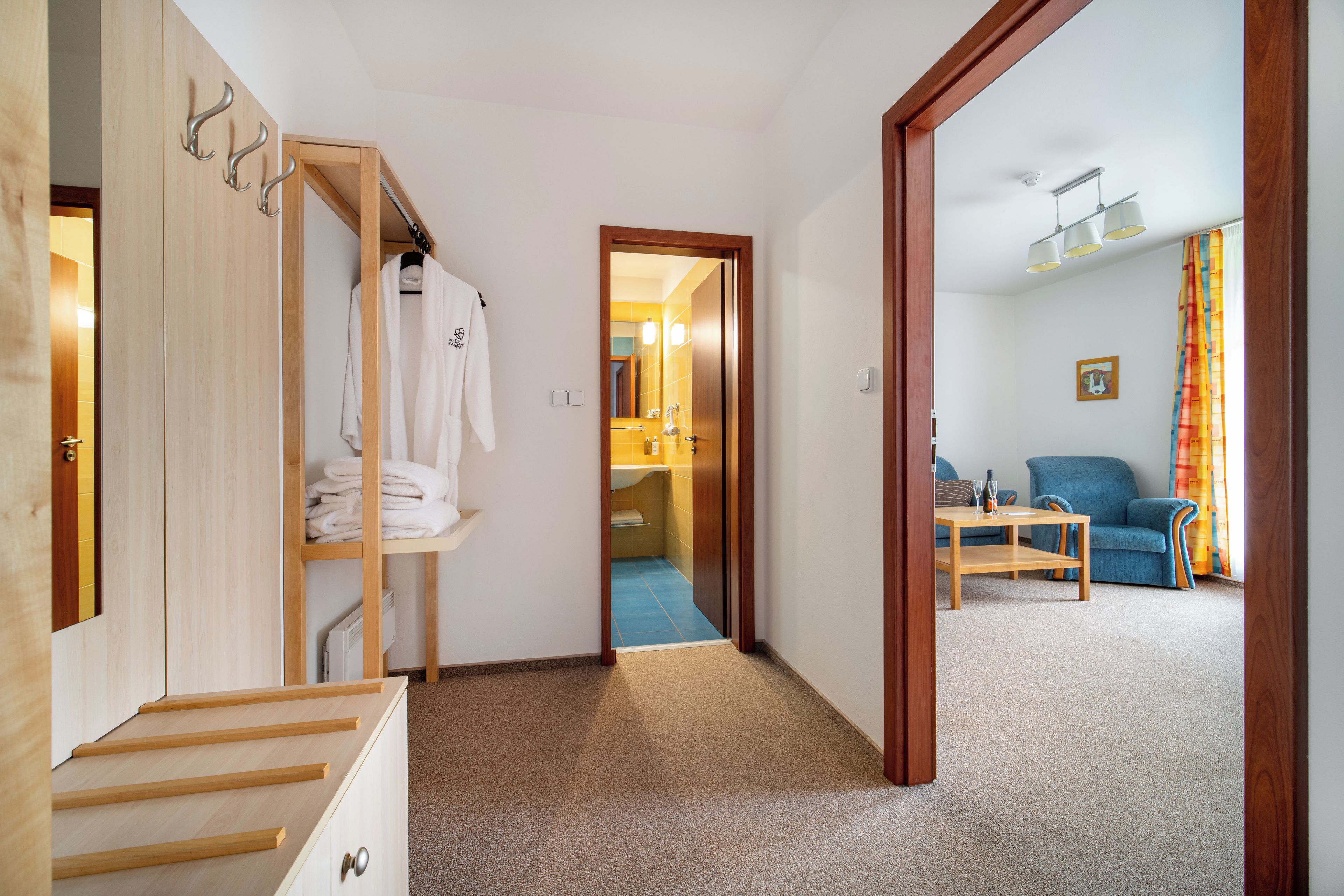 Un pasillo que conduce a un baño con ducha, una escalera de madera y una sala de estar con sofá y mesa.