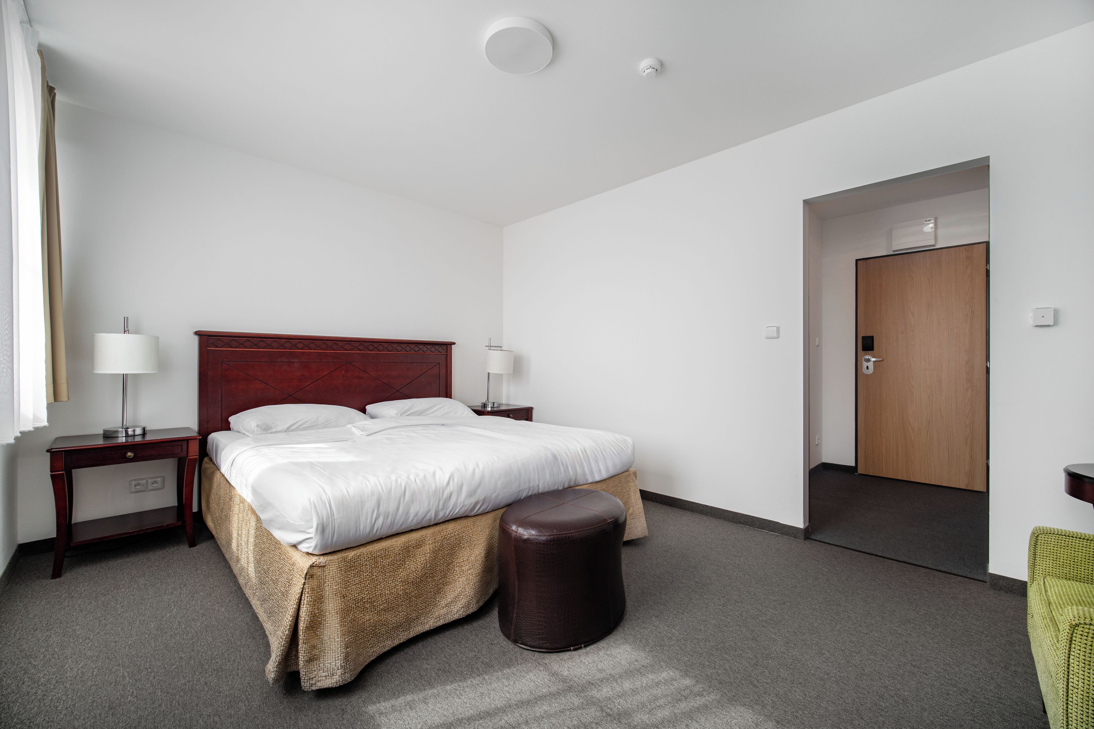 A hotel room with a large bed, two bedside tables with lamps, a wooden wardrobe, and a door leading to another room.