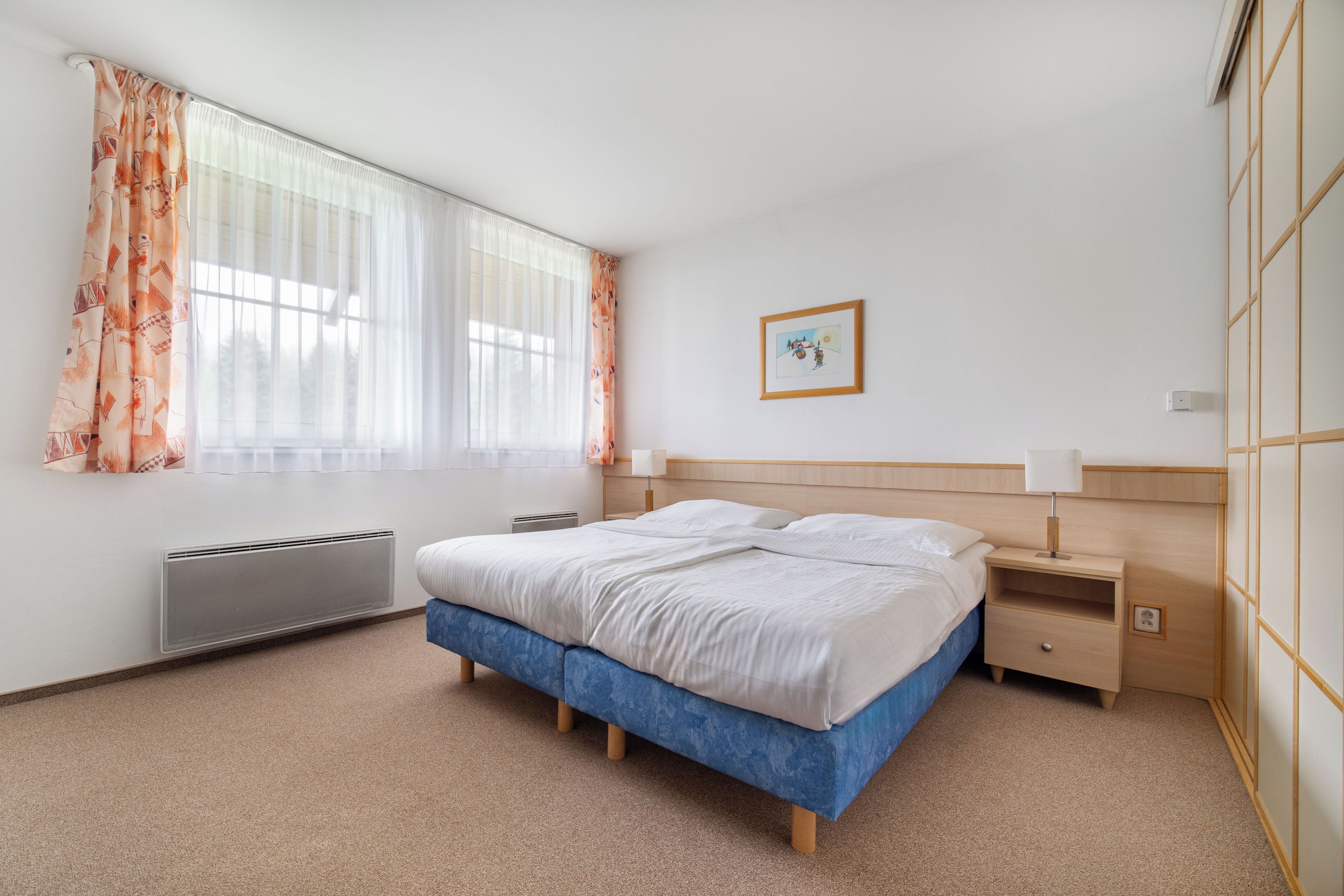 Un dormitorio con una cama, una mesita de noche, un radiador y una ventana con cortinas.