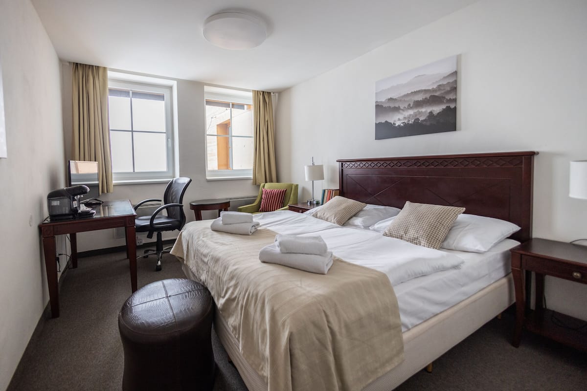 A hotel room with a large bed, a desk, a chair, a lamp, and a painting on the wall.