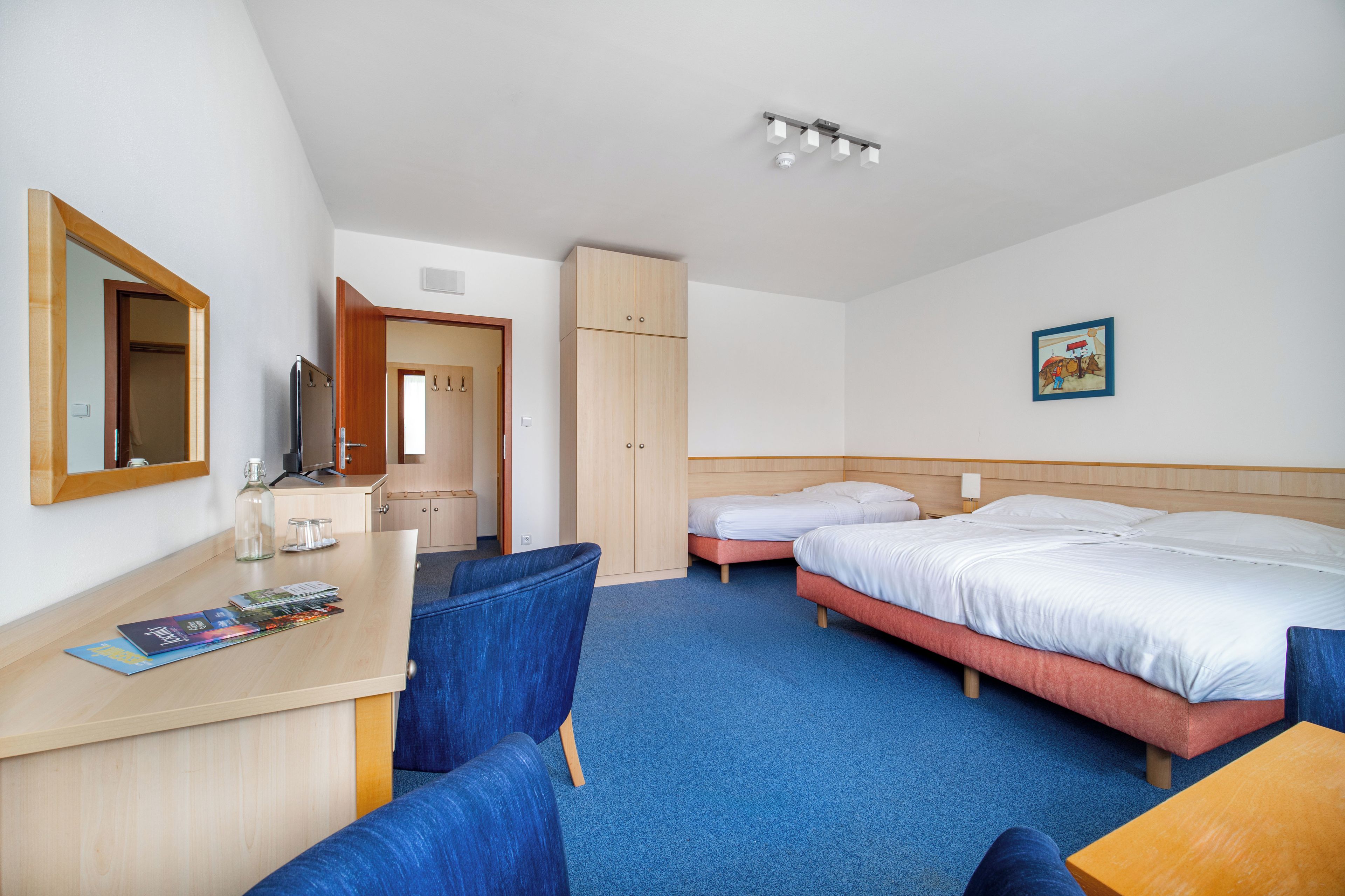 A hotel room with a desk, two beds, a wardrobe, and a mirror.