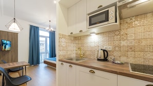 Una cocina moderna con armarios blancos, un microondas y un lavabo. Hay una mesa de comedor con sillas y un televisor montado en la pared.