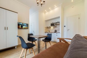 A modern living room with a sofa, a dining table with chairs, a TV mounted on the wall, and a kitchen area with cabinets and a microwave. - Scandinavian Apartments (Kyiv)