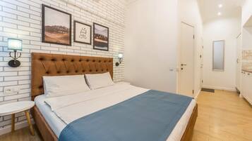 A bedroom with a large bed, white brick wall, two framed pictures, bedside lamps, and a small round table.