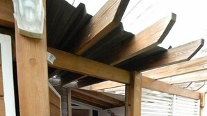 A wooden deck with a pergola, a dining area with chairs and a table, and a window with blinds. - Bougainvillier, pool, direct access to the beach (Grand Fond)