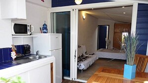 A compact kitchen with a microwave, a coffee maker, and a refrigerator. A wooden table and chairs are in the dining area, and a bed is visible through an open door. - Bougainvillier, pool, direct access to the beach (Grand Fond)