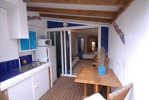 A compact kitchen with a microwave, sink, and blue cabinets. There is a wooden dining table with chairs and a vase of dried plants.