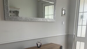 Una habitación con una consola de madera, un espejo grande de marco texturizado y una puerta con ventanal.