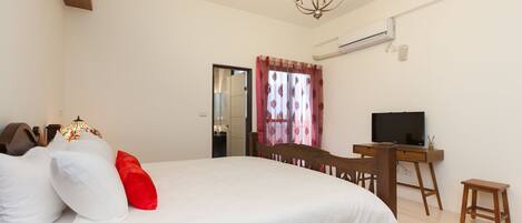 A bedroom with a bed, a desk, a television, and an air conditioning unit.